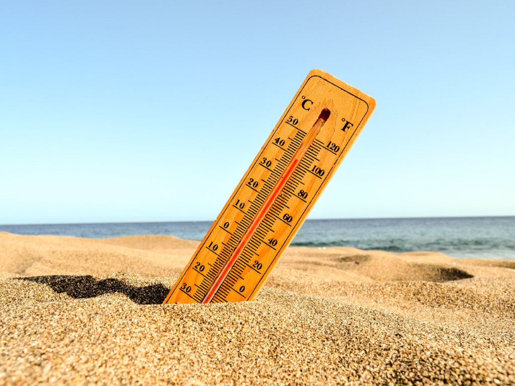 A wooden thermometer stuck in the sand on the beach, showing a high temperature